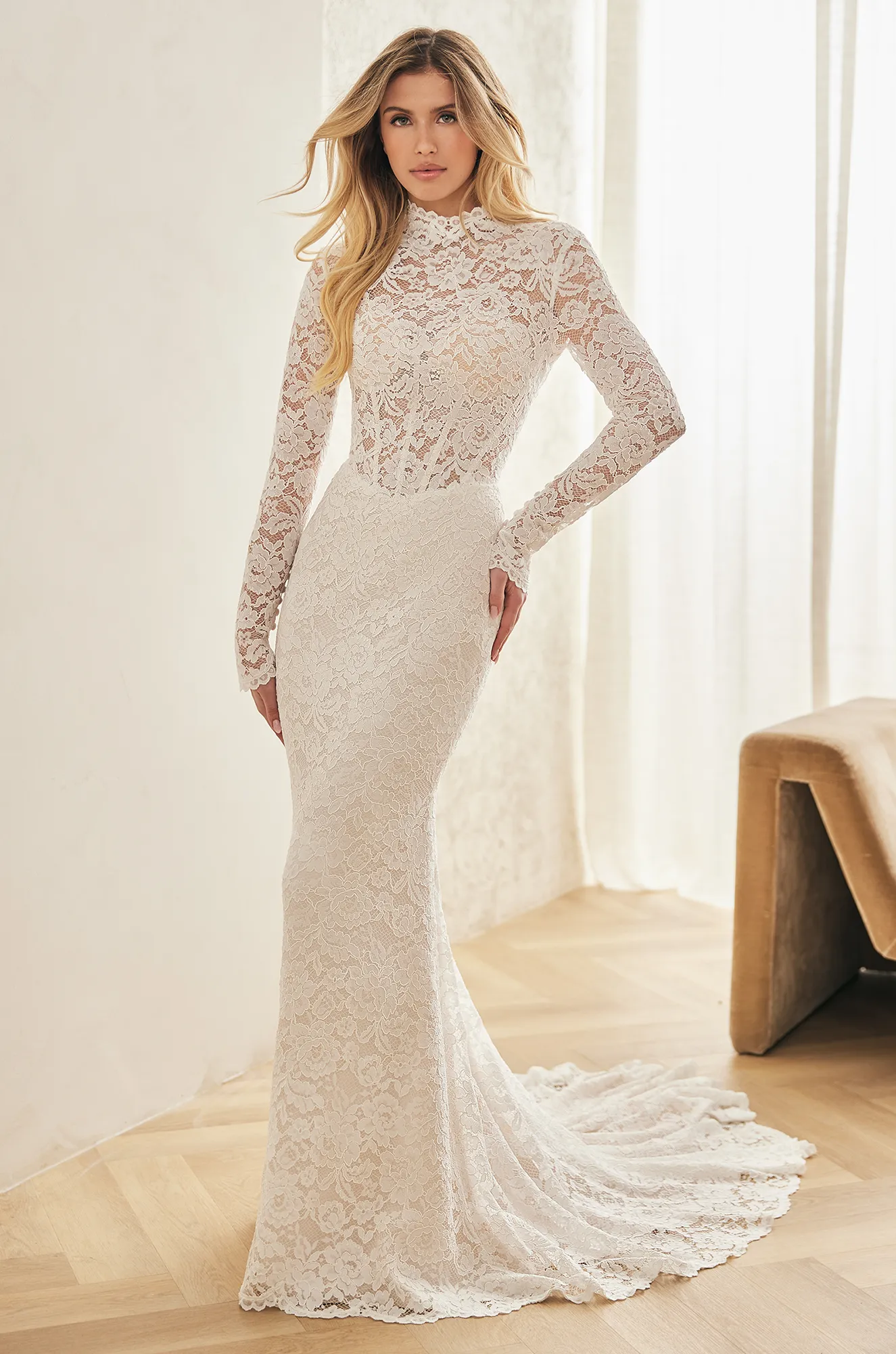 Front view of a lace wedding dress with a sheer bodice, high neckline, long lace sleeves and a basque waist, with a lace fit and flare skirt, in a ballroom.