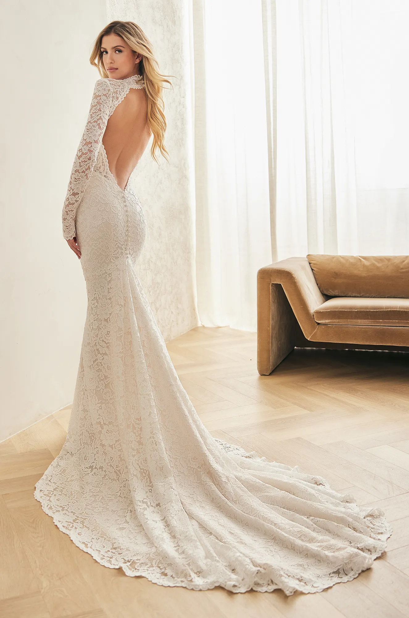 Back view of a lace wedding dress with long lace sleeves and an open key-hole back, with a fit and flare lace skirt and buttons on back of dress to end of zipper, in a ballroom.