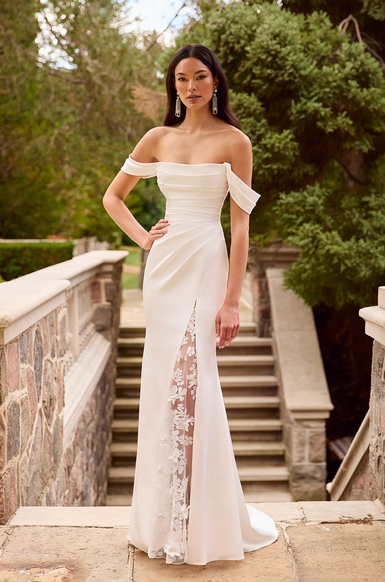 Off-the-shoulder fitted gown with ruched bodice, side slit lined with floral lace, and floor-length train.