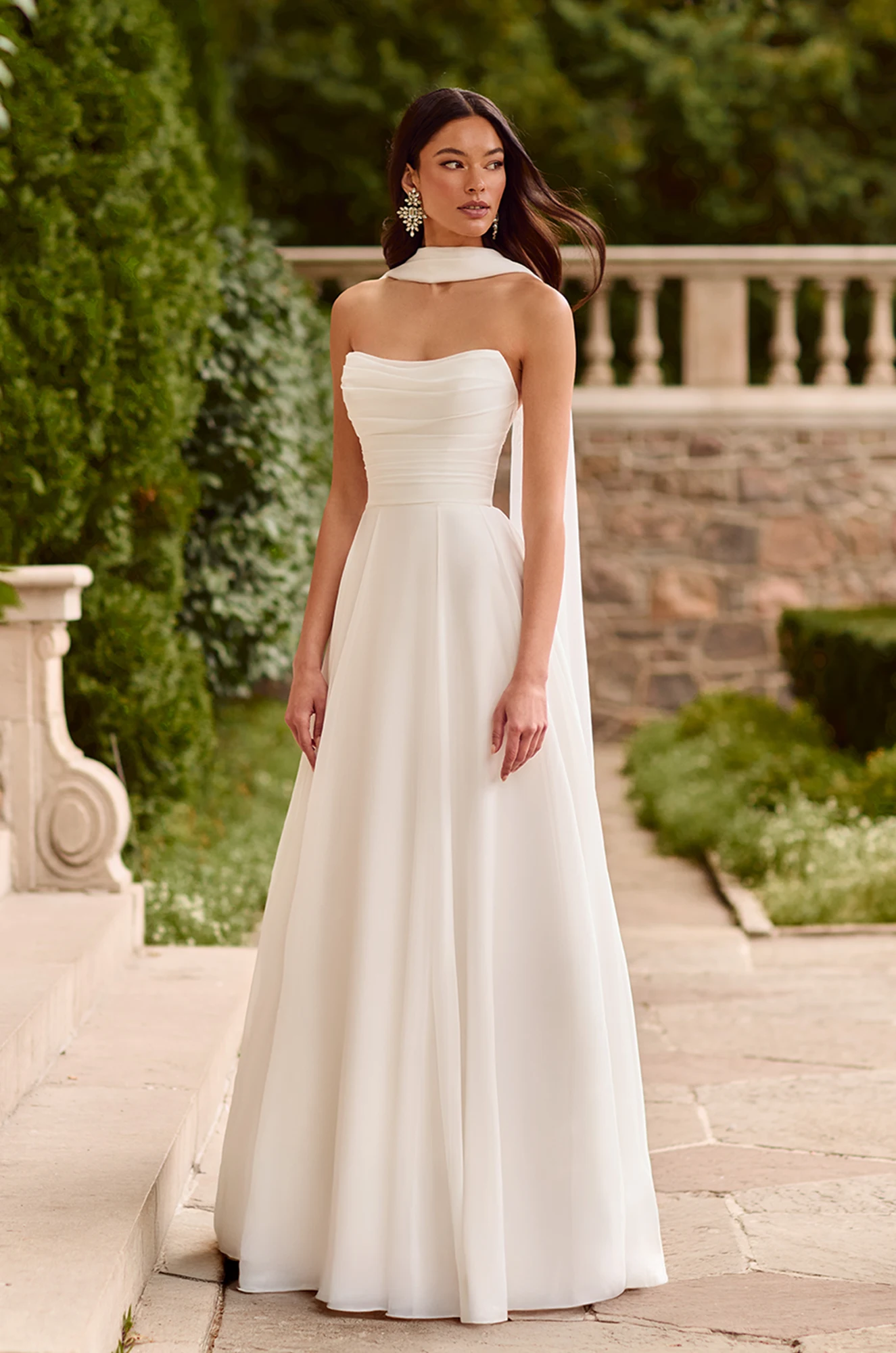 Strapless A-line gown with ruched bodice, soft chiffon skirt, and an elegant neck scarf flowing down the back.
