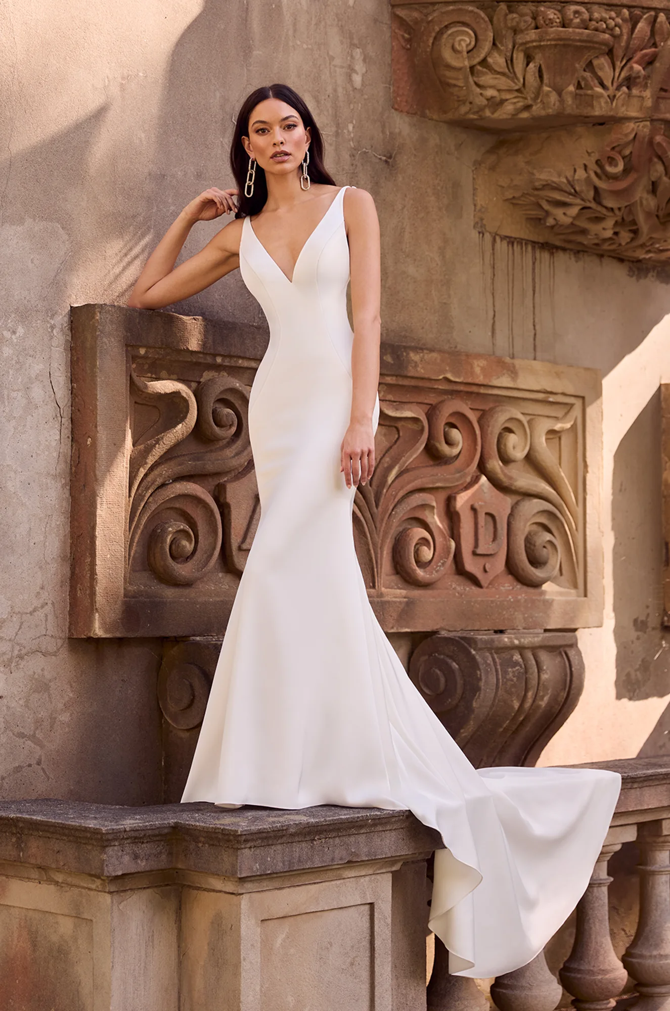 Crepe mermaid gown with deep V-neckline, contoured seams, low back, and sweeping train for a sleek bridal silhouette.
