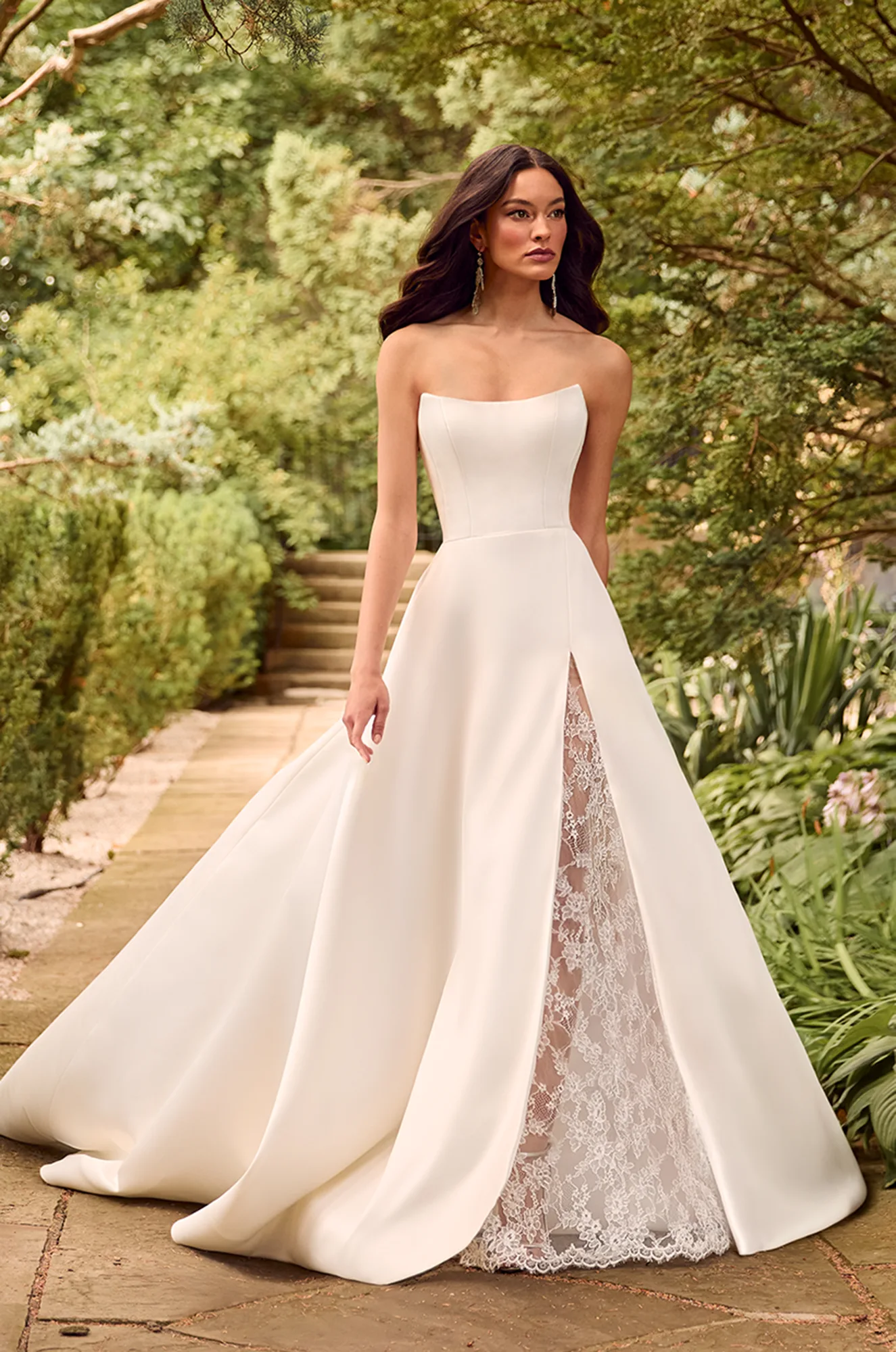 Strapless A-line gown with structured bodice and front slit revealing delicate lace underlay.