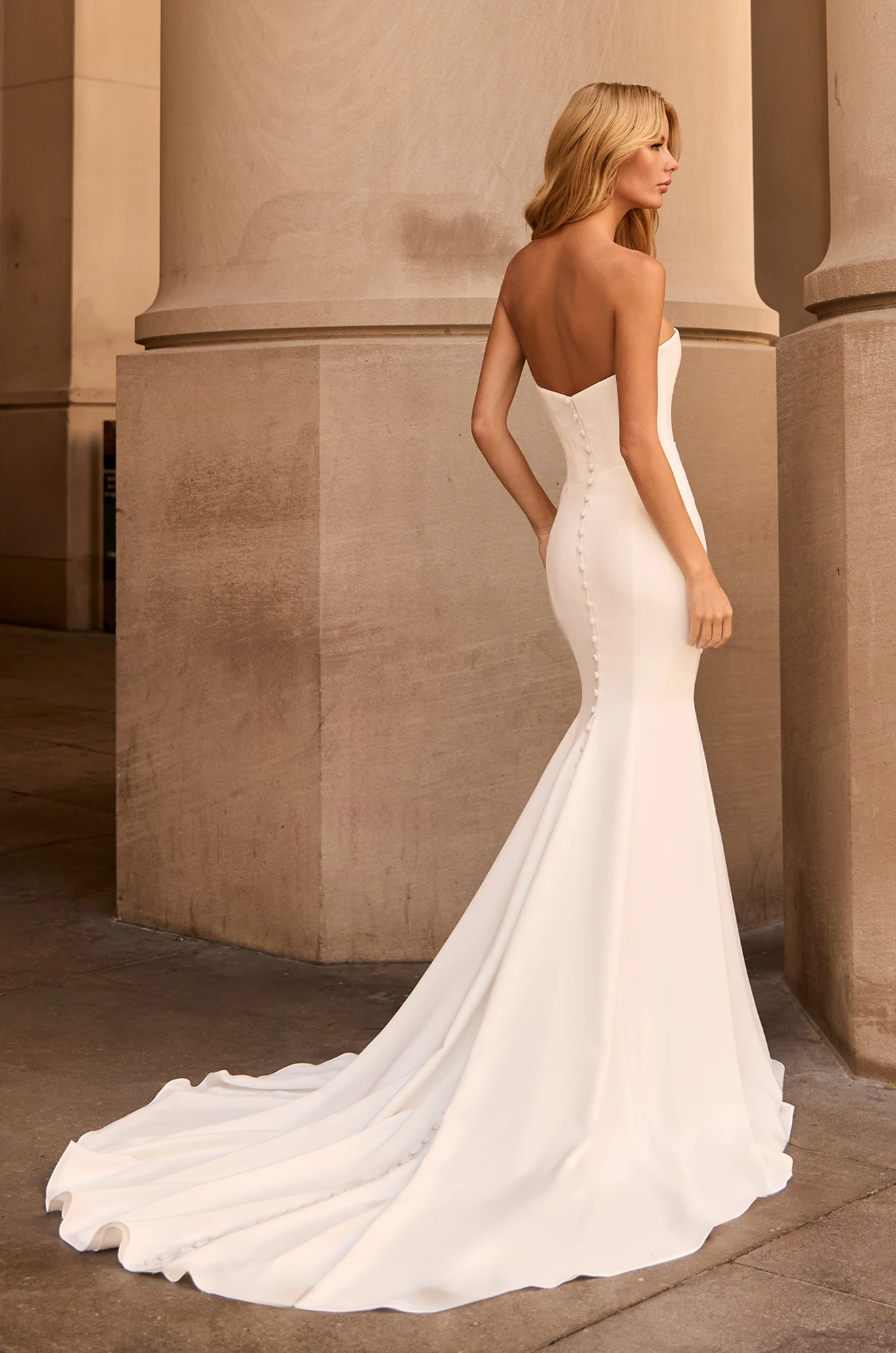 Back view of strapless Crepe wedding dress with buttons down back to hem of train, fit and flare Crepe skirt, outside of a building.