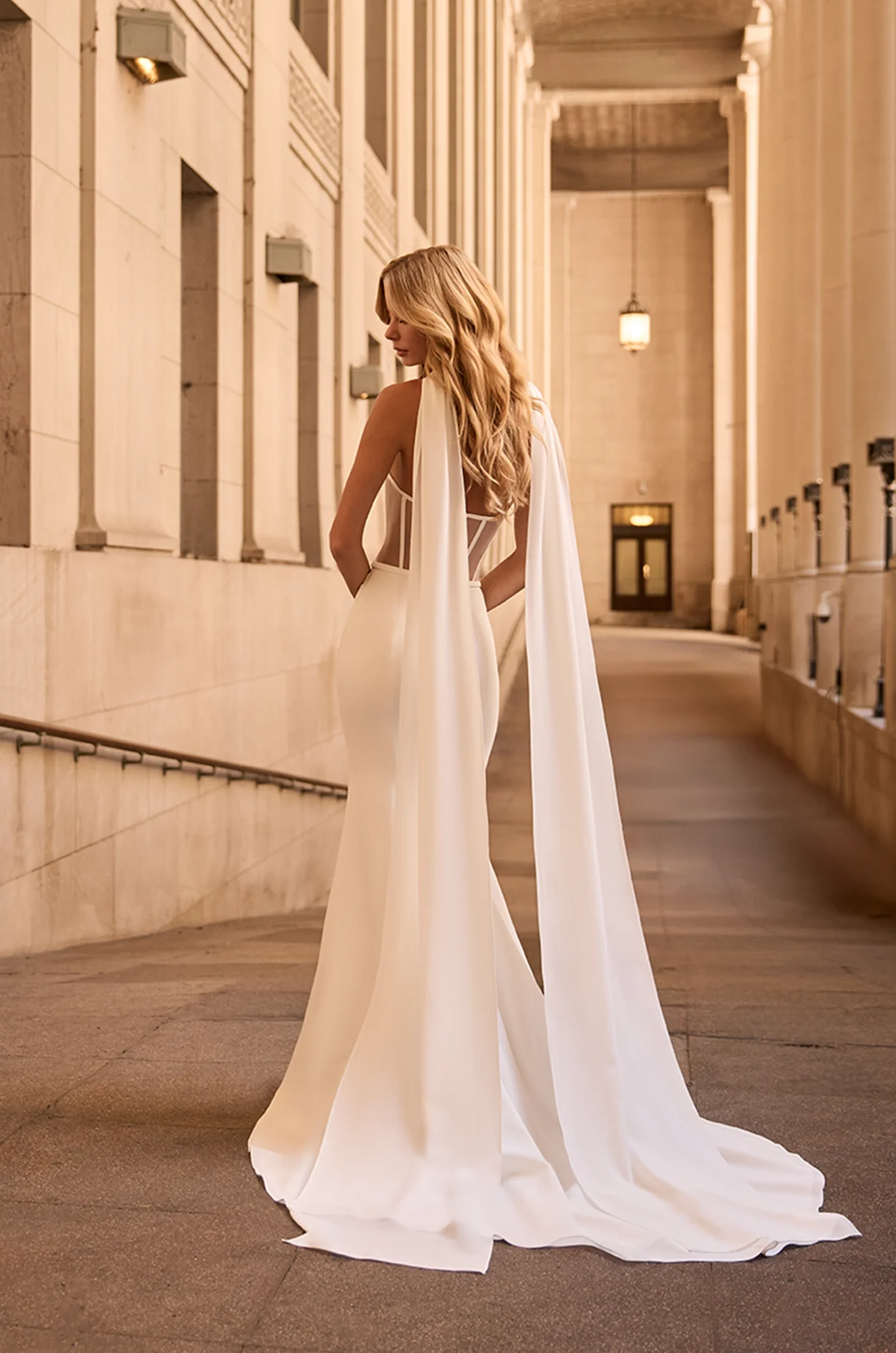 Back view of strapless Crepe wedding dress with scarf at back over shoulders, with exposed boning on back of bodice outside of a building.