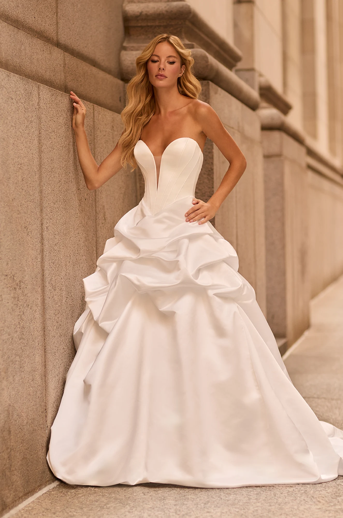 Strapless ball gown with deep sweetheart neckline, fitted corset bodice, and layered satin skirt featuring dramatic ruffle details.