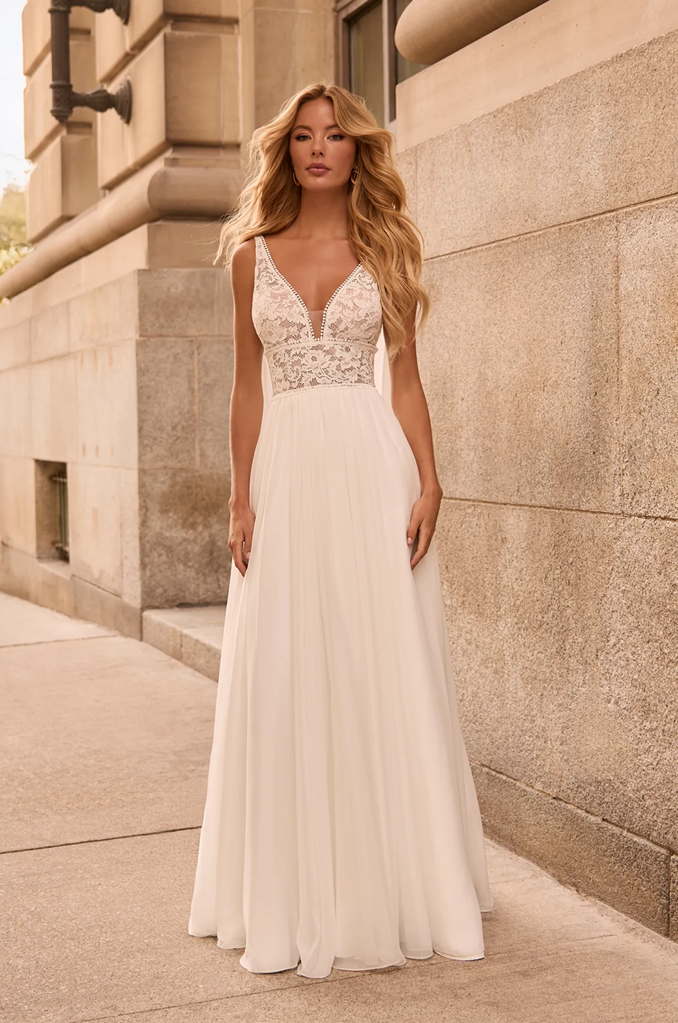 Romantic sleeveless gown with deep V-neck lace bodice, sheer detailing, defined waist, and light chiffon skirt in soft ivory.