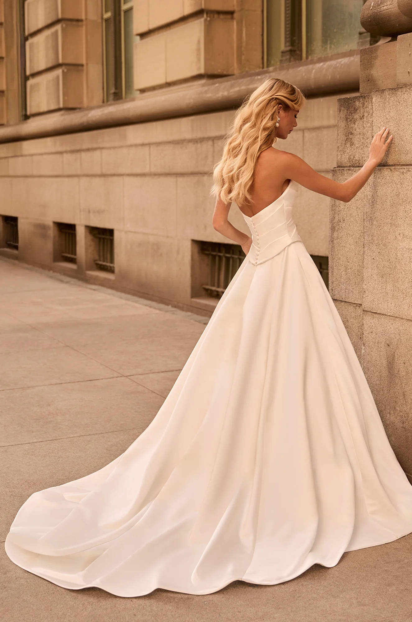 Back view of strapless Satin wedding dress with buttons on back of bodice to waist and A-line skit, outside of a building.