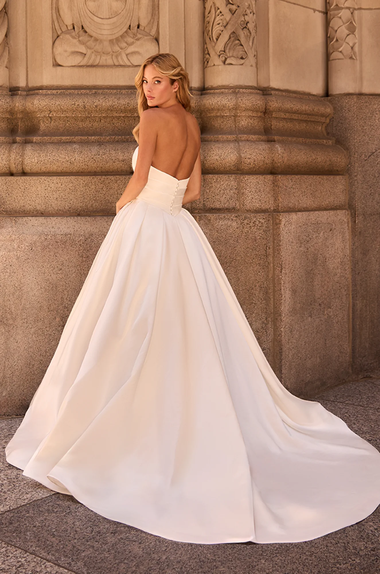 Back view of strapless Satin ball gown wedding dress with buttons down back to waist and open back, outside of a building.