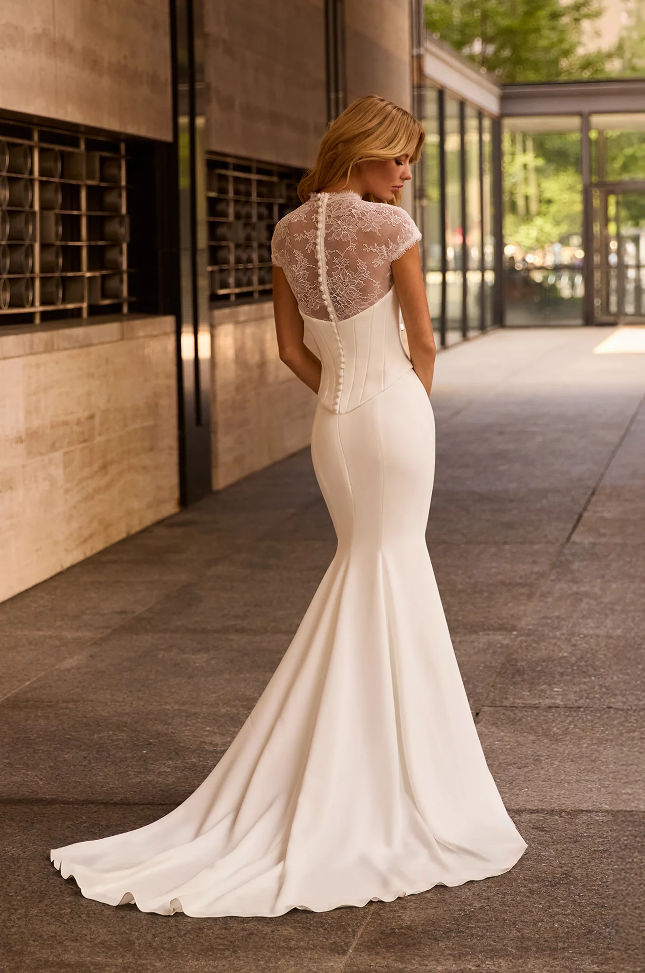 Back view of two piece fit and flare Crepe and lace wedding dress with buttons down back of bodice, outside of a building.