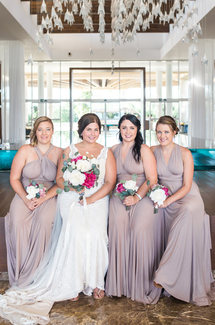  Bride in a fit and flare lace gown stands next to bridesmaids in light purple, holding matching bouquets.