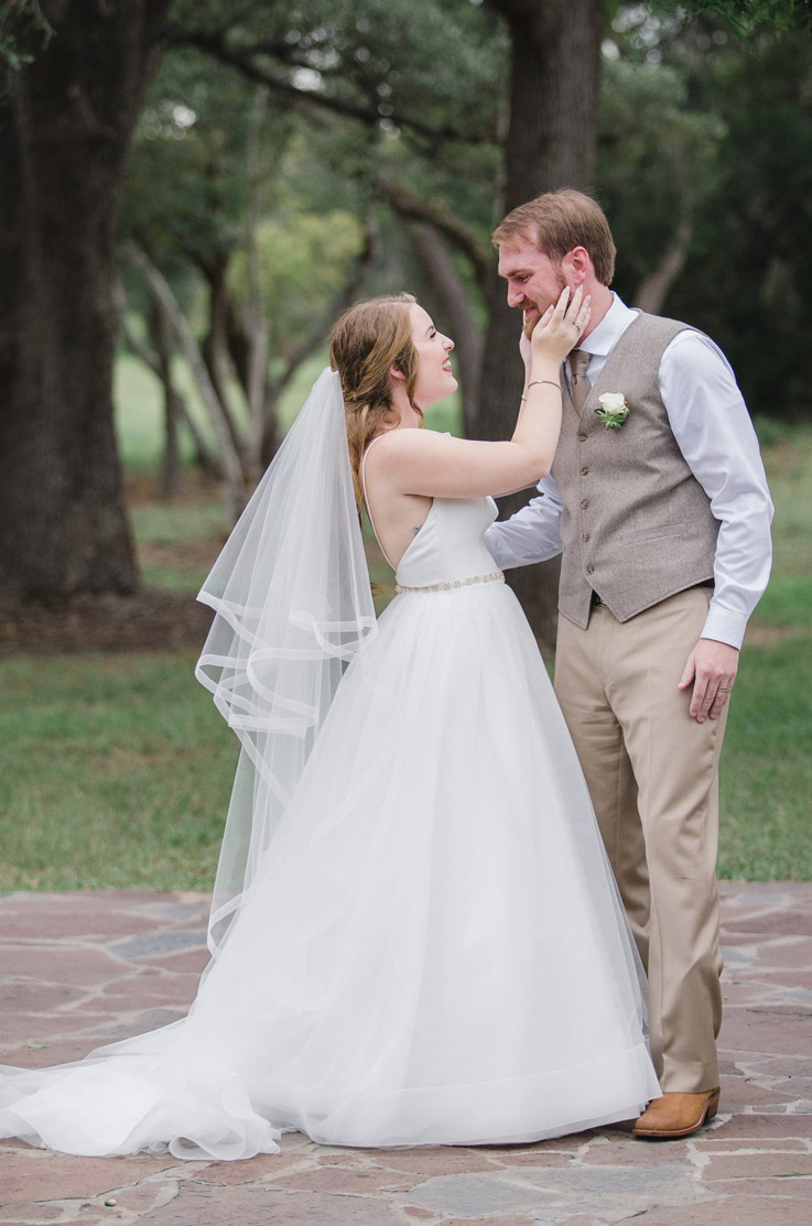 Bride faces groom in a tulle ballgown with a veil, a crepe bodice and a beaded belt, standing on a path outdoors.