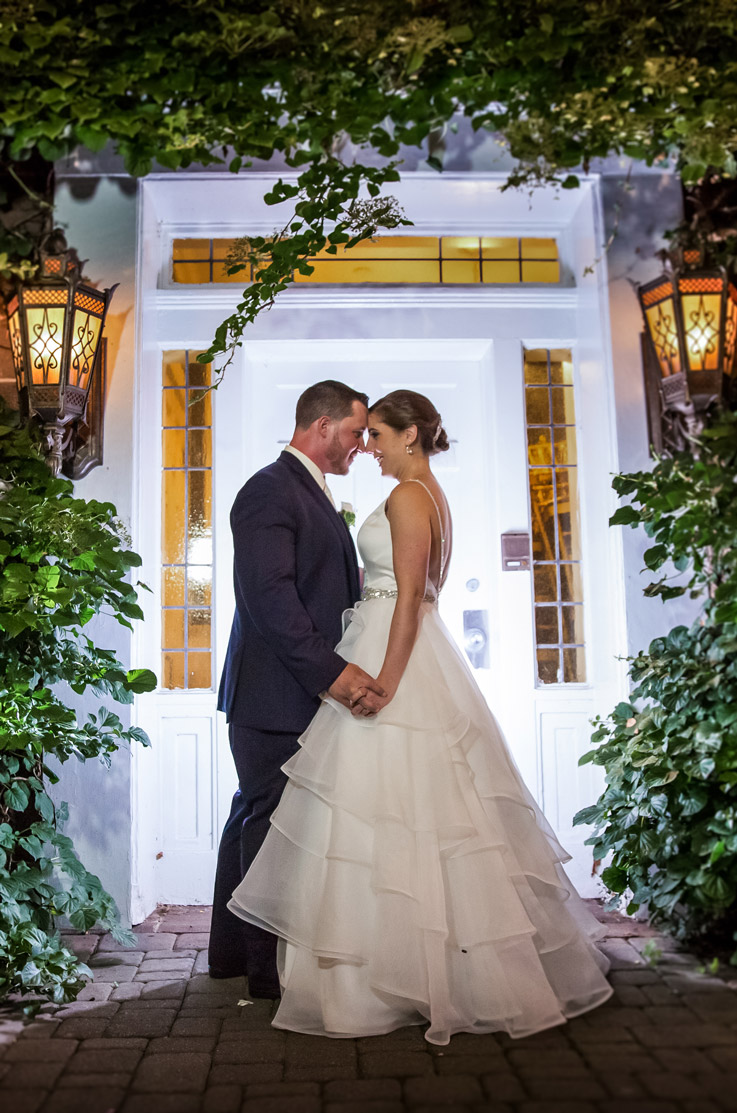 Bride in a layered organza ballgown with a satin bodice and belt detail, faces groom and they hold hands at venue entrance.