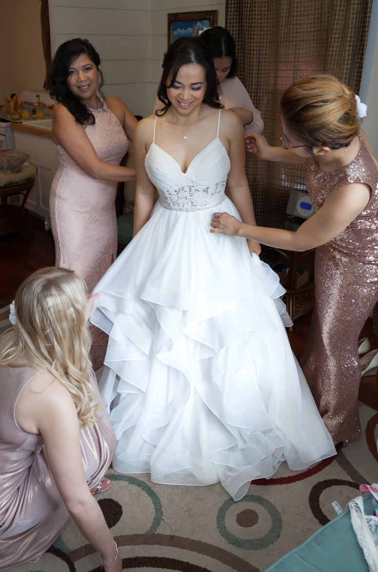 Bride in a V-neck tulle bodice wedding dress with lace and a layered skirt,  gets ready with her bridesmaids in bridal suite.