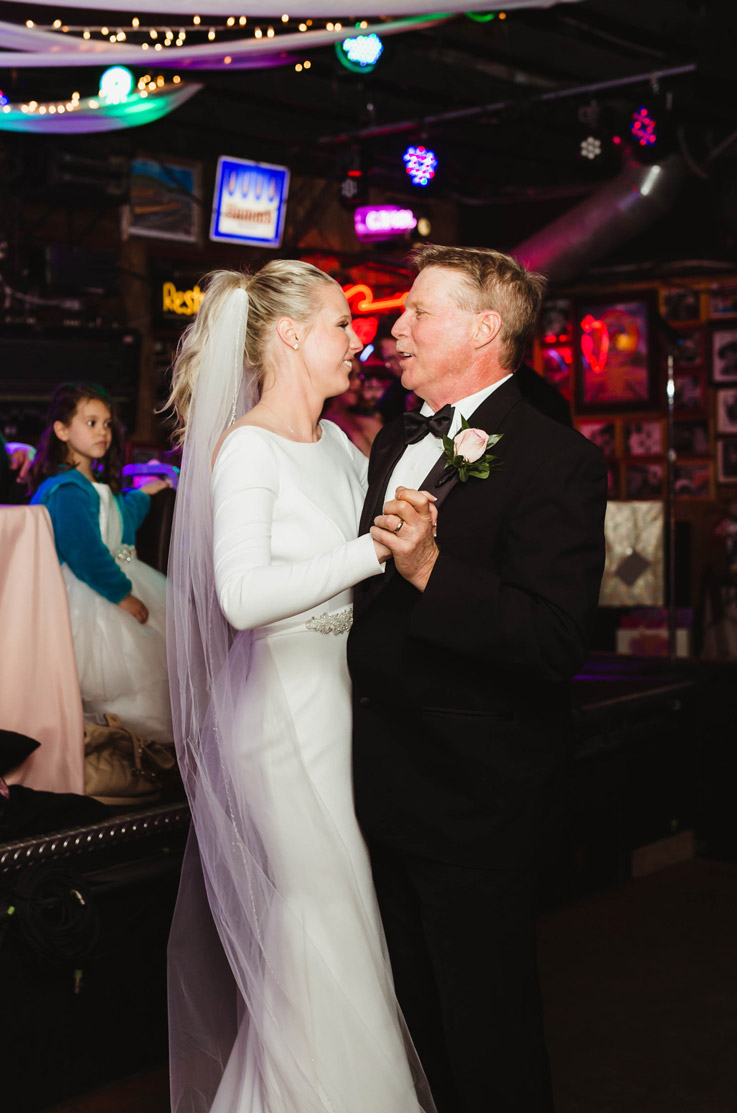 Bride in a crepe fit and flare gown with a bateau neck, a veil and belt detail dances with her father during the reception.