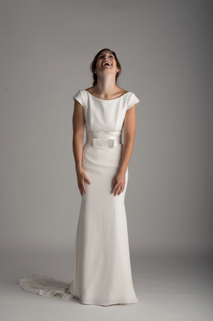 Bride in a crepe bateau neck wedding dress with cap sleeves and a wide belt, photographed in a studio setting.