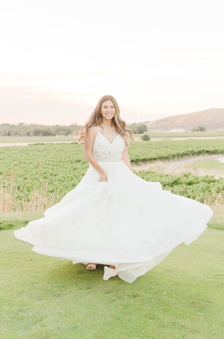 Bride wearing a layered tulle wedding dress with a lace bodice and spaghetti straps, twirling in a sunlit vineyard.