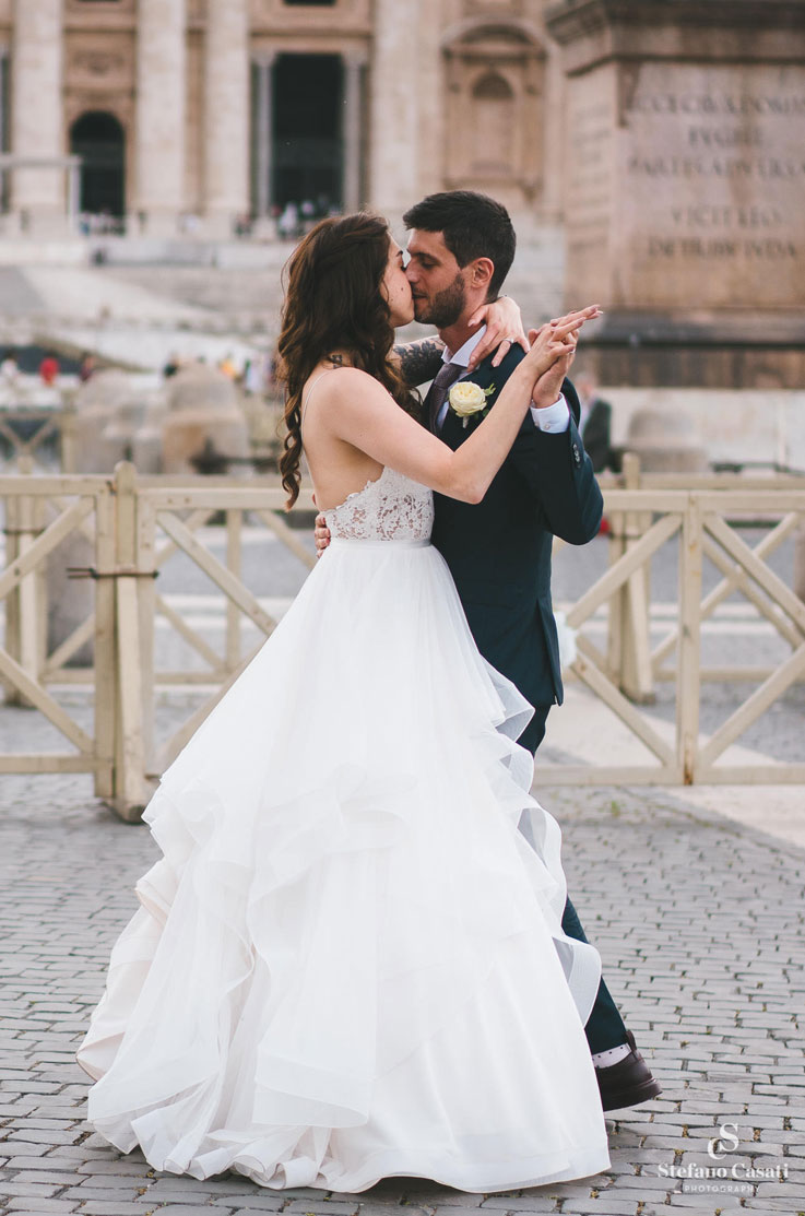 Bride in a multi-layered tulle wedding gown with a lace bodice, dances with groom and they kiss, on city street in Rome.