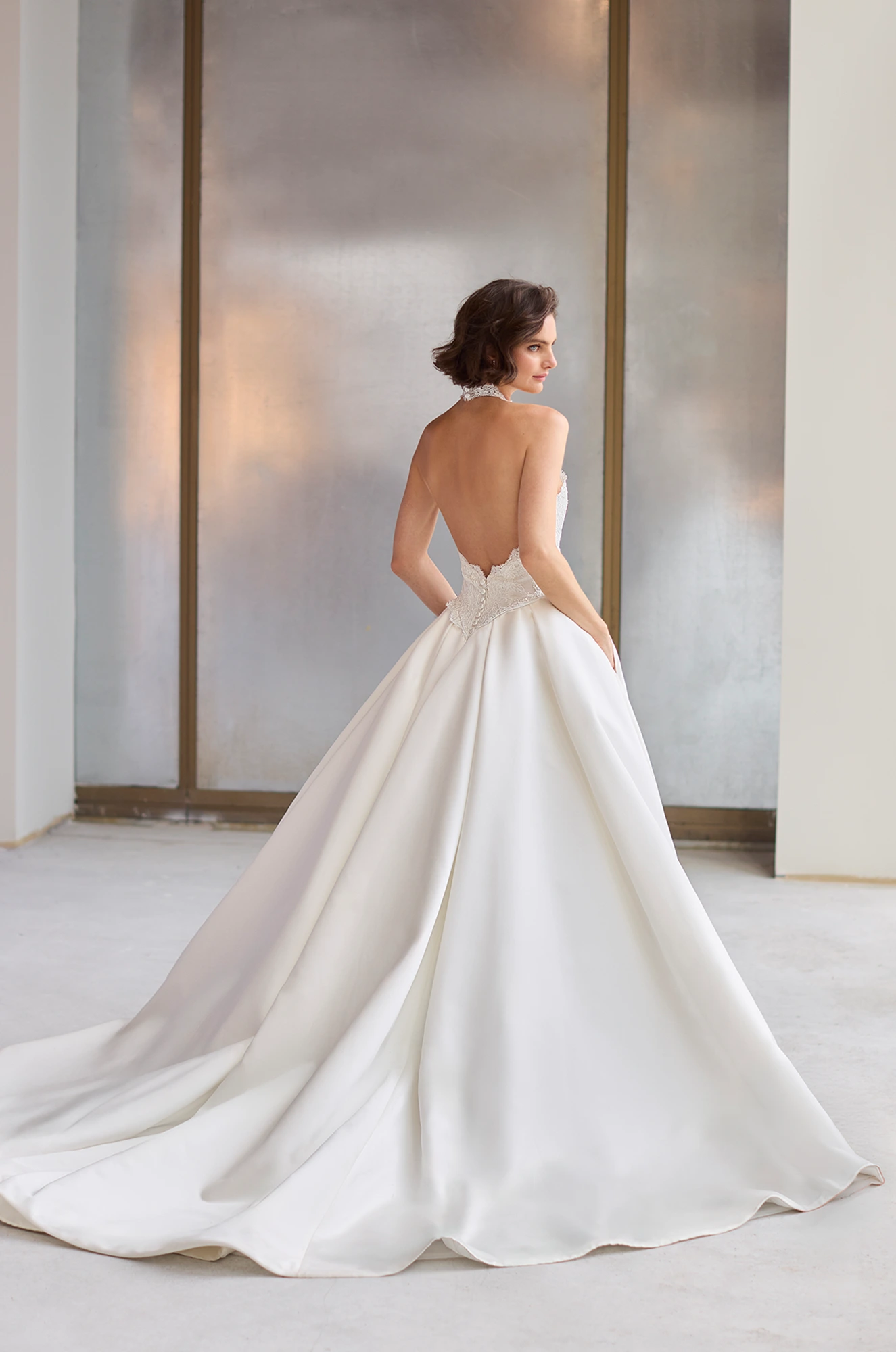 Back view of a backless wedding dress with a Lace bodice and full Satin A-line skirt, in a studio.