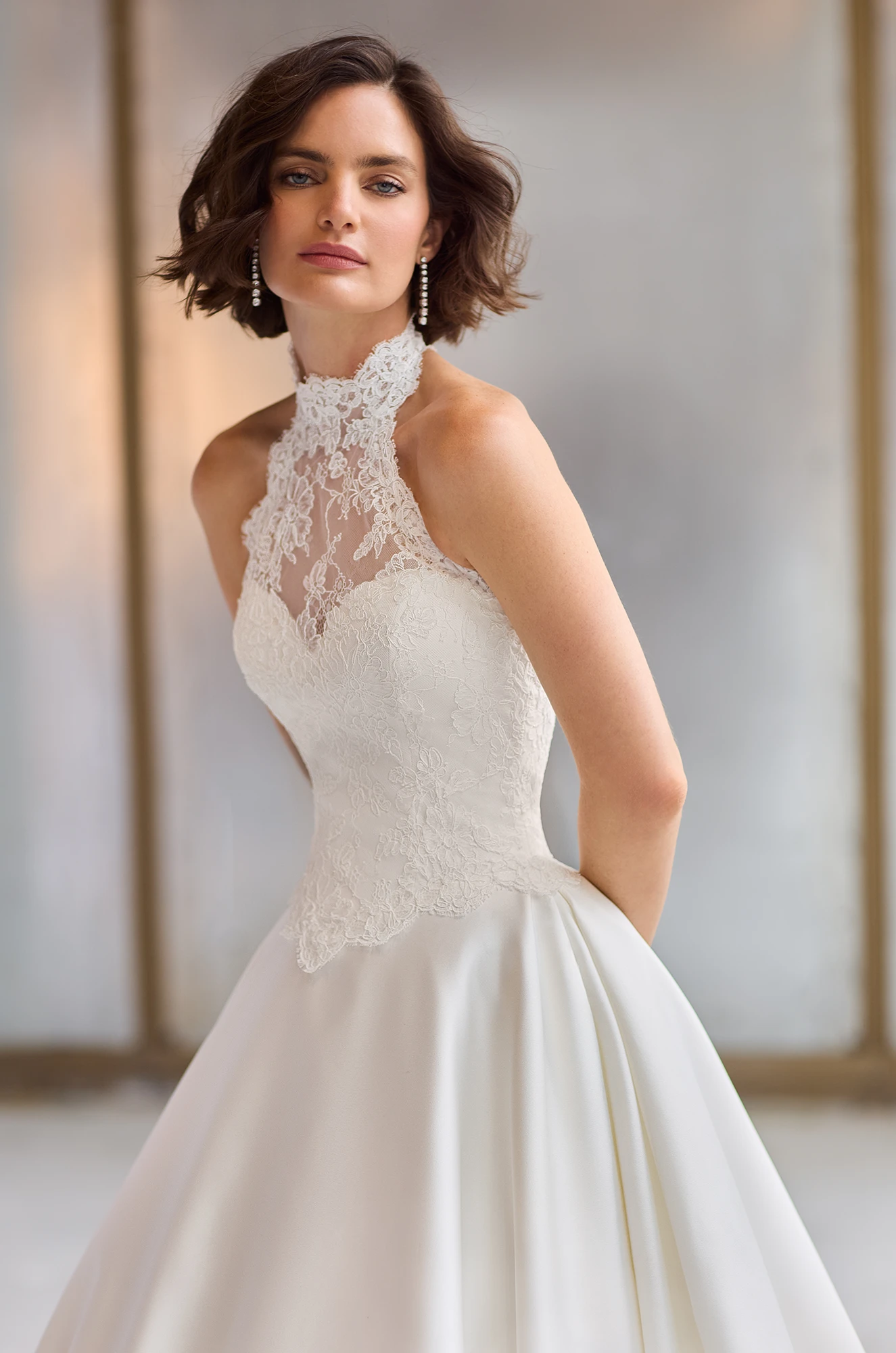 Close up view of a halter neckline wedding dress with a Lace bodice and full Satin A-line skirt, in a studio.