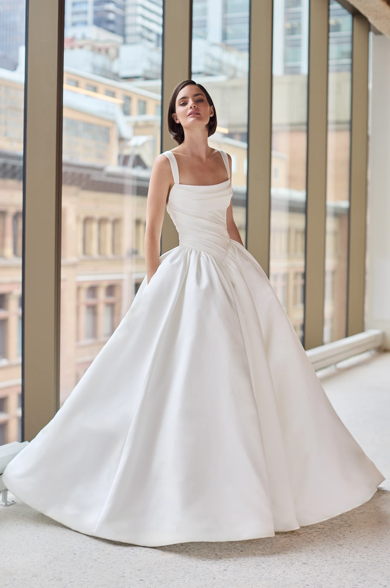 Satin gown with a sleeveless draped bodice, basque waistline, and gathered ball gown skirt with pockets.