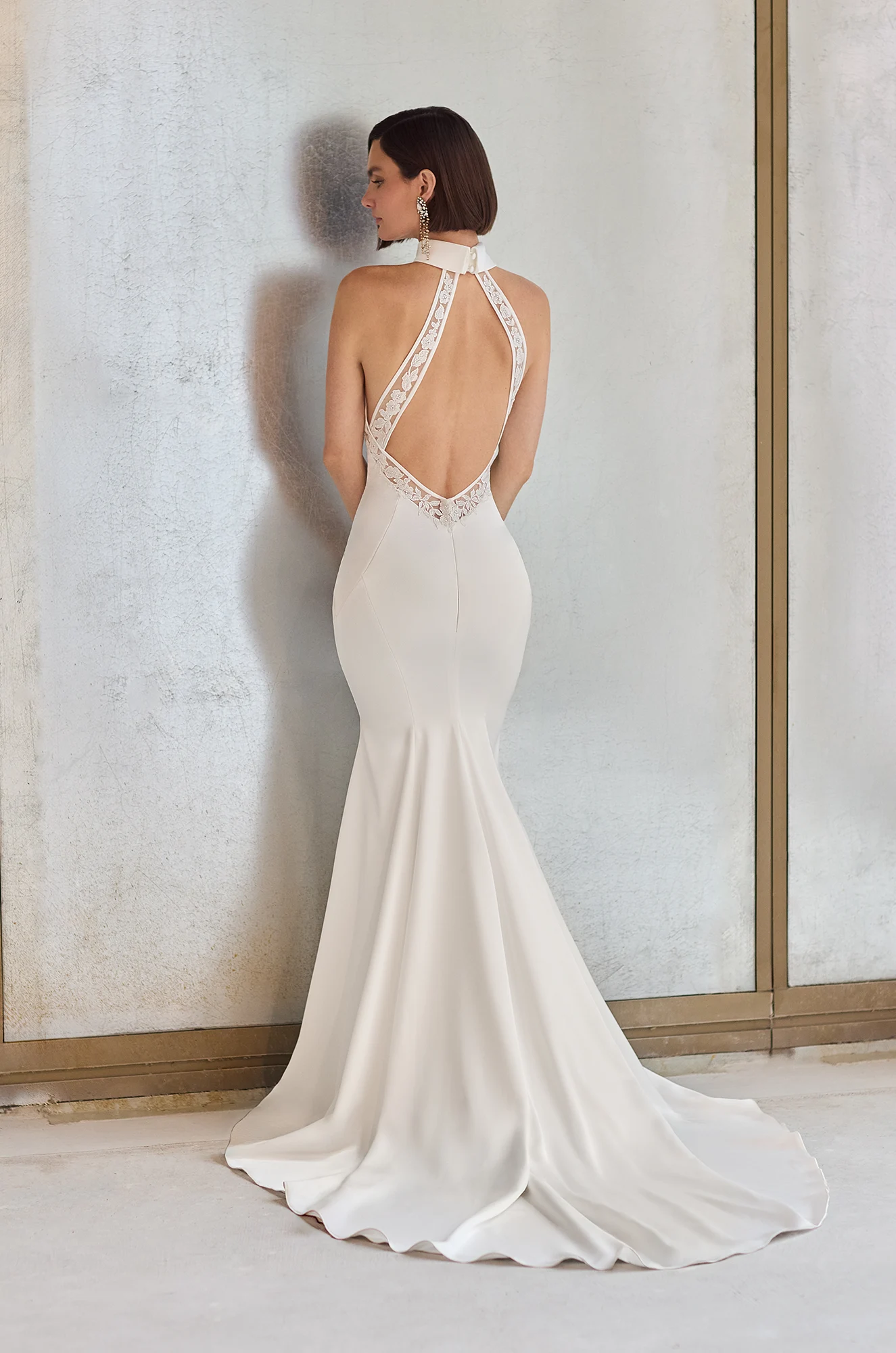 Back view of a fitted Charmeuse wedding dress with illusion Lace detail along the sides of the bodice and on the back straps, in a studio.