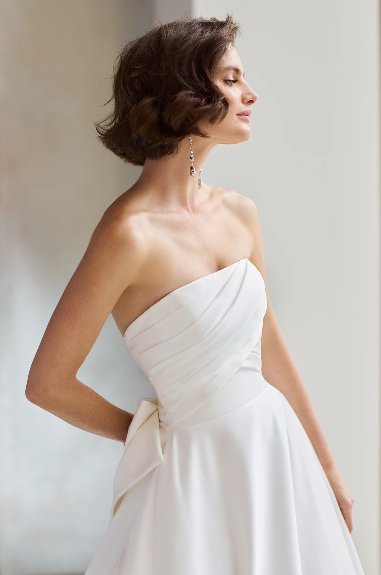 Close up view of a strapless Satin wedding dress with a pleated bodice an A-line skirt and a bow on the back of the dress, in a studio.