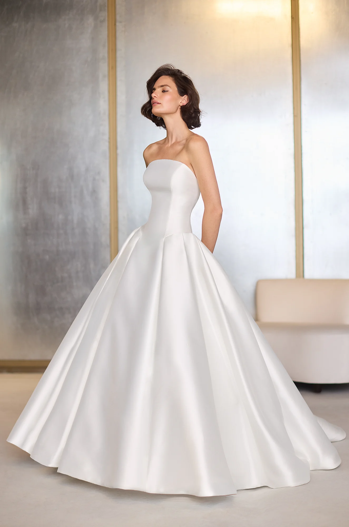 Front view of a strapless Mikado princess cut wedding dress with an arched neckline and box pleated ball gown skirt, in a studio.