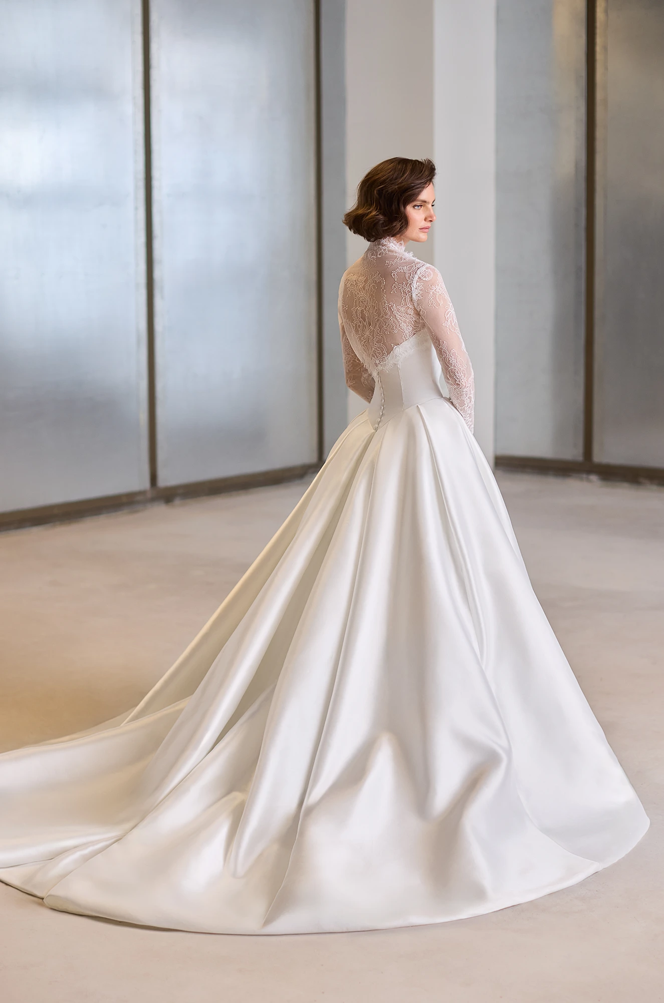 Back view of a strapless Mikado wedding dress with a box pleated ball gown skirt, with a removable long sleeve sheer Lace bolero, in a studio.