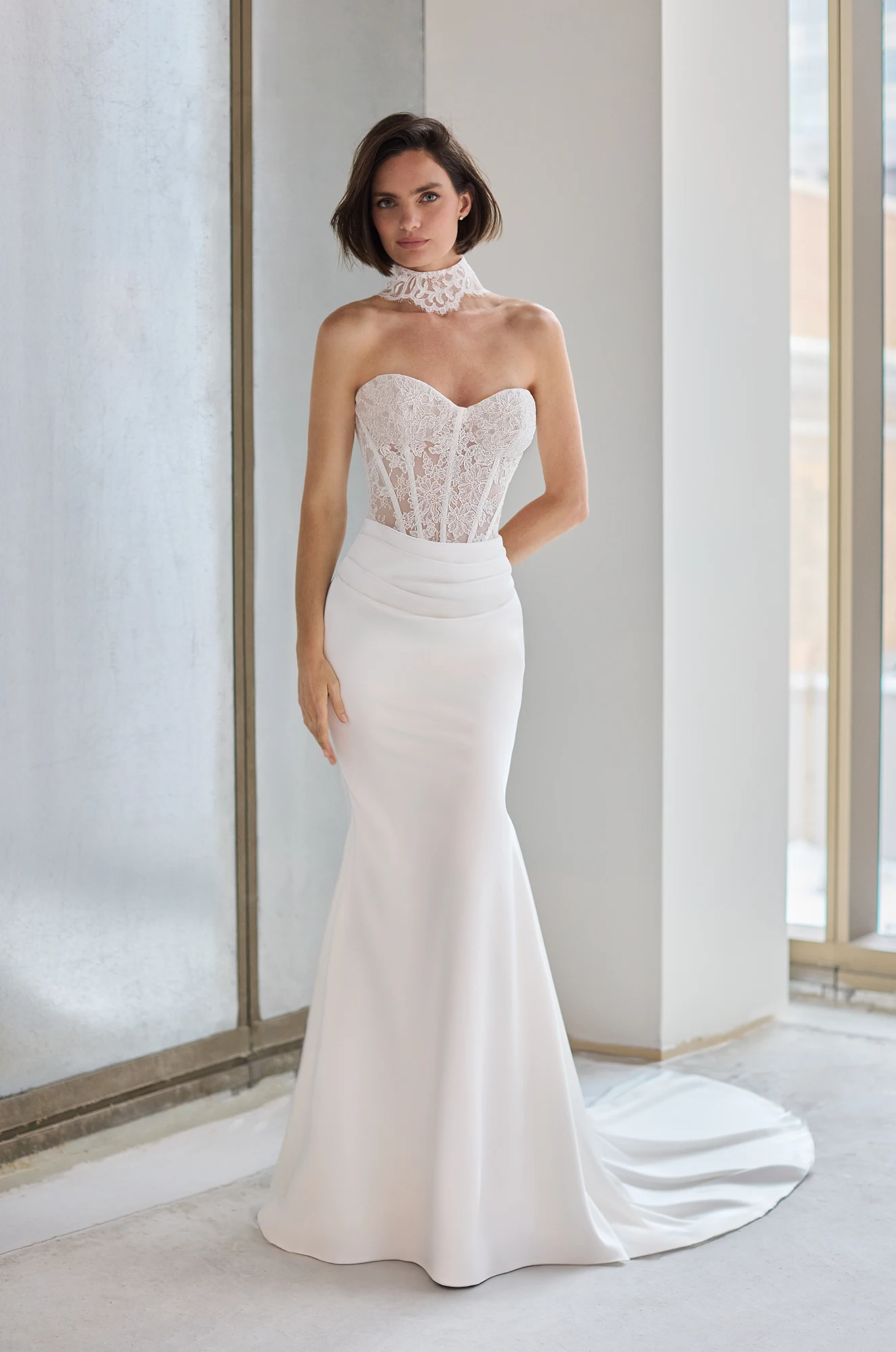 Front view of a strapless wedding dress with a sheer Lace bodice, a draped fit and flare Charmeuse skirt, and a Lace choker, in a studio.