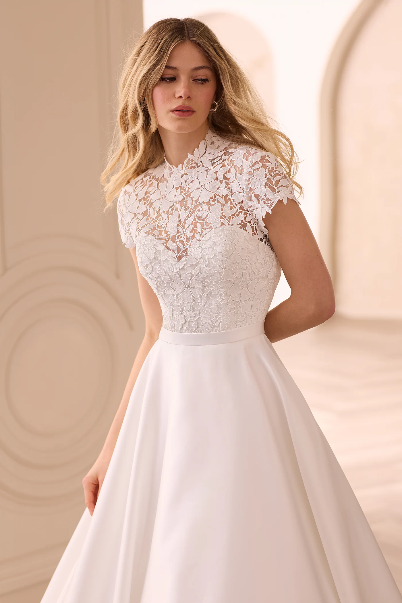 Close up view of a jewel neckline wedding dress with a Lace bodice and cap sleeves, with a sweetheart neckline on lining and a Satin A-line skirt in front of a doorway.