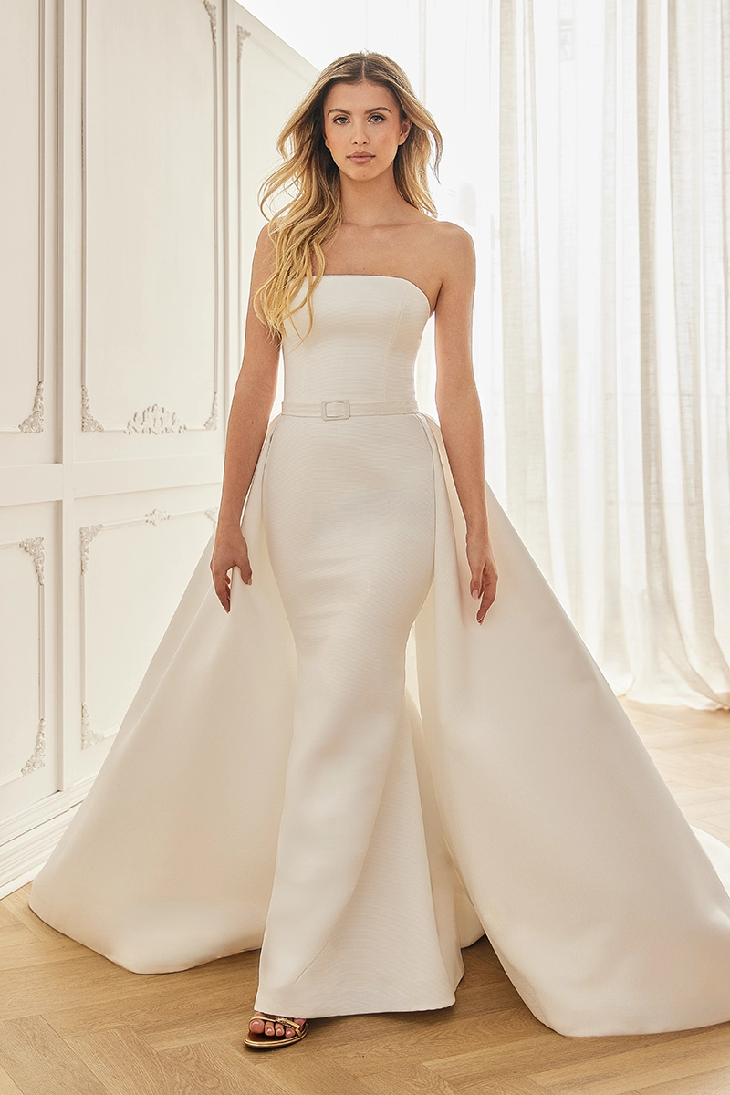 Satin wedding dress with a straight neckline, fit and flare silhouette, detachable overskirt and belt detail.