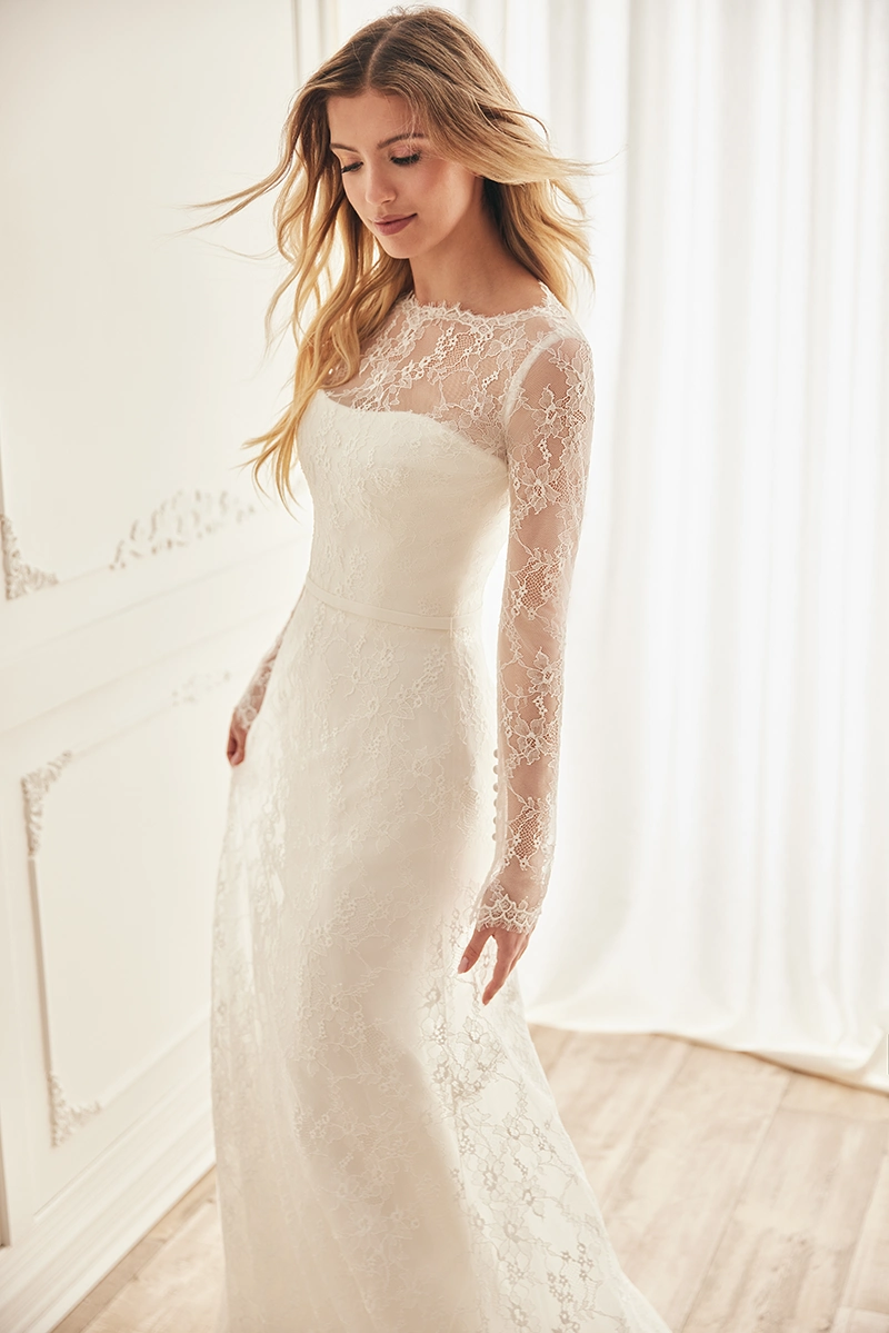 Long-sleeve floral lace wedding gown with illusion neckline, fitted bodice and full lace overlay, photographed in soft light.