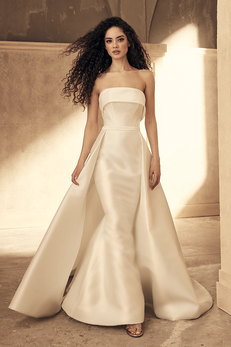 Strapless mermaid gown with wide banded neckline, sleek fitted bodice, and dramatic overskirt creating a regal silhouette.