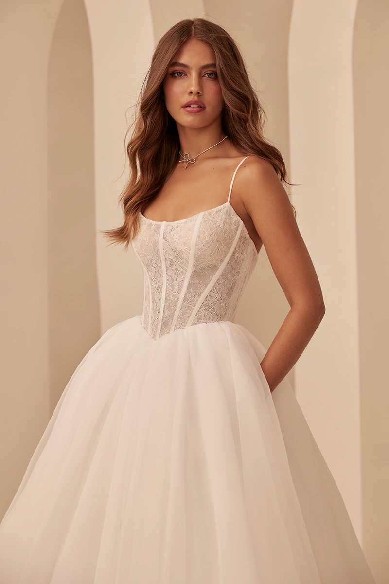 Ball gown wedding dress with lace corset bodice, thin straps and full tulle skirt, photographed in a light modern studio.