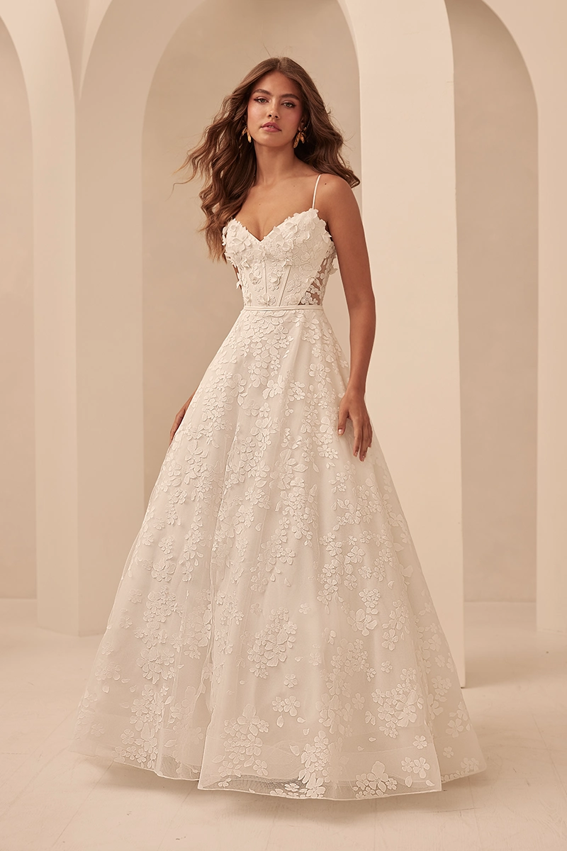 Floral appliqué A-line gown with sheer corset bodice, delicate straps, and skirt featuring 3D blossom detailing.