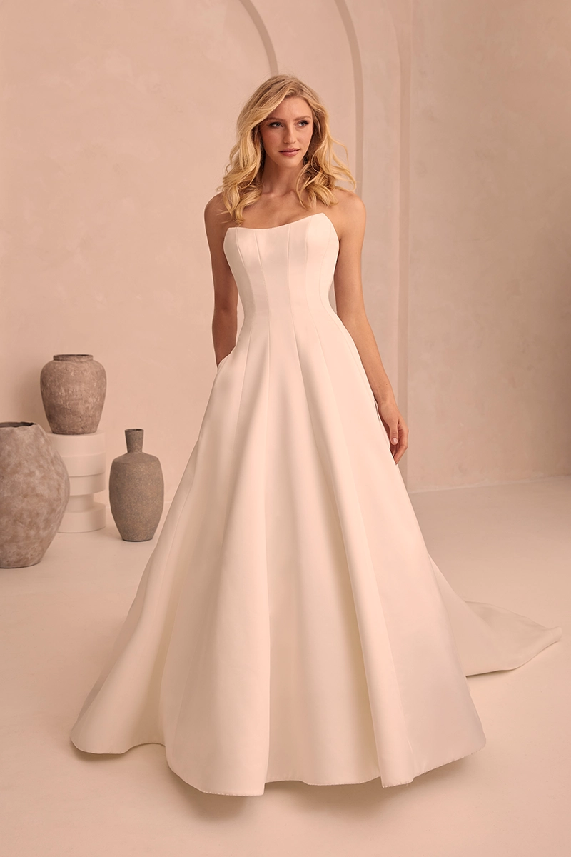 Modern strapless wedding gown featuring a fitted paneled bodice, and voluminous A-line skirt in satin fabric.