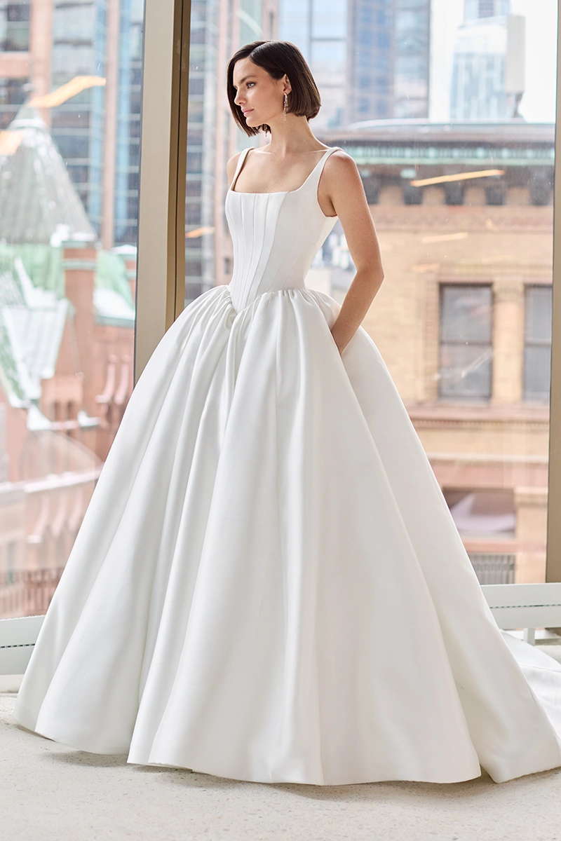 Mikado gown with a square neckline, sleeveless seamed bodice, basque waistline, and gathered ball gown skirt with pockets.