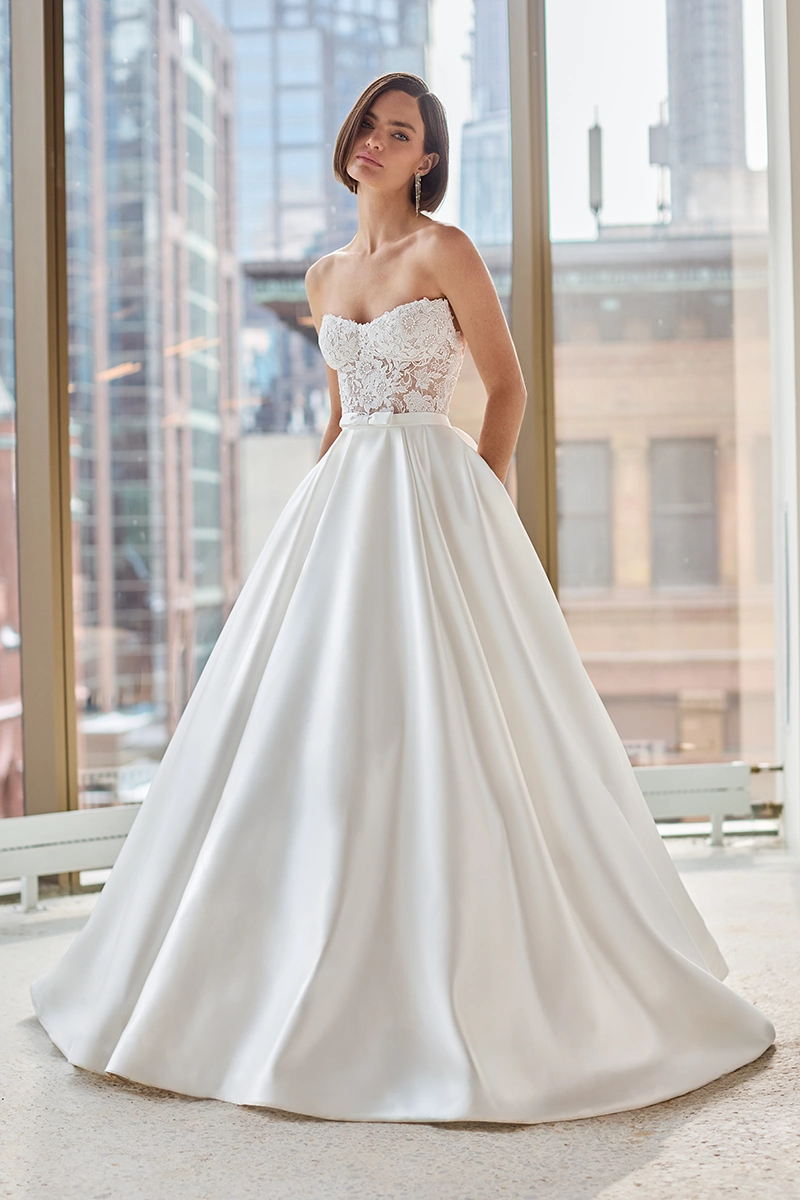 Lace gown with strapless sheer Lace bodice, band with bow at waist, and a full satin ball gown overskirt.