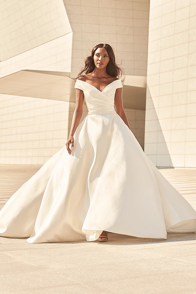 Off-the-shoulder Mikado ball gown with a draped bodice and full circle skirt, photographed outdoors with modern architecture.