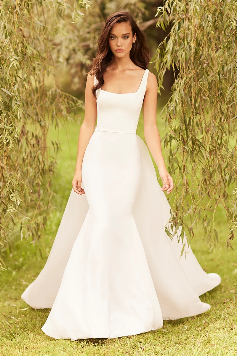 Square-neck crepe gown with fit and flare skirt and detachable overskirt, shown outdoors.