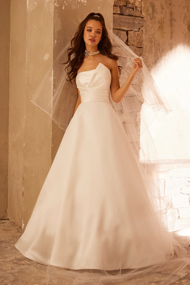 Strapless Mikado A-line gown with asymmetrical draping, ruched waist, and flowing skirt shown with sheer veil.