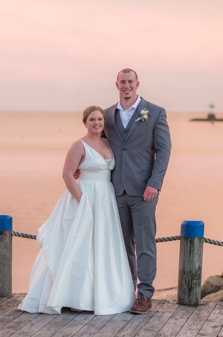 Bride in a V-neck silk ballgown with beaded detail on the bodice, poses with groom on a waterfront dock at sunset.