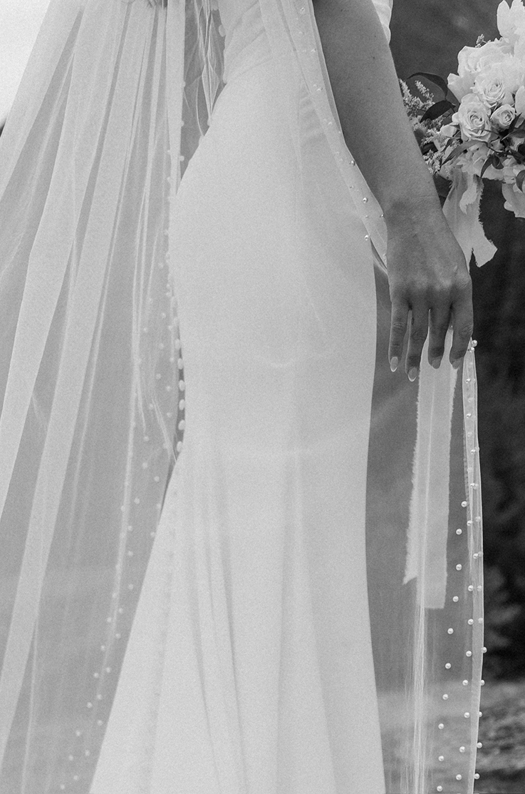 Close-up of bride in a fit and flare gown with a buttoned back and a veil with pearls, and a rose bouquet in black and white.