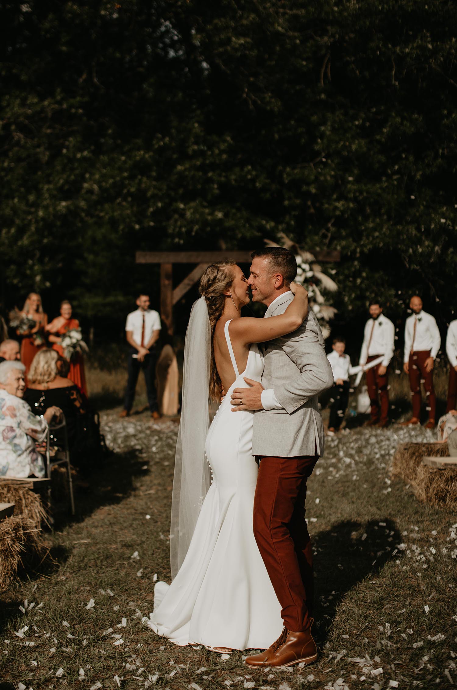 Bride in a fit and flare low back wedding dress with buttons and a veil, kisses groom in front of the altar and seated guests. 