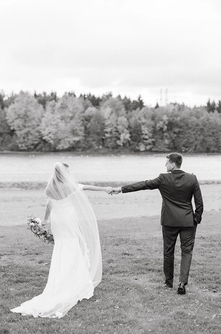 Bride in a charmeuse satin fit and flare gown with sleeves and a veil, poses with groom in an open field in black and white.