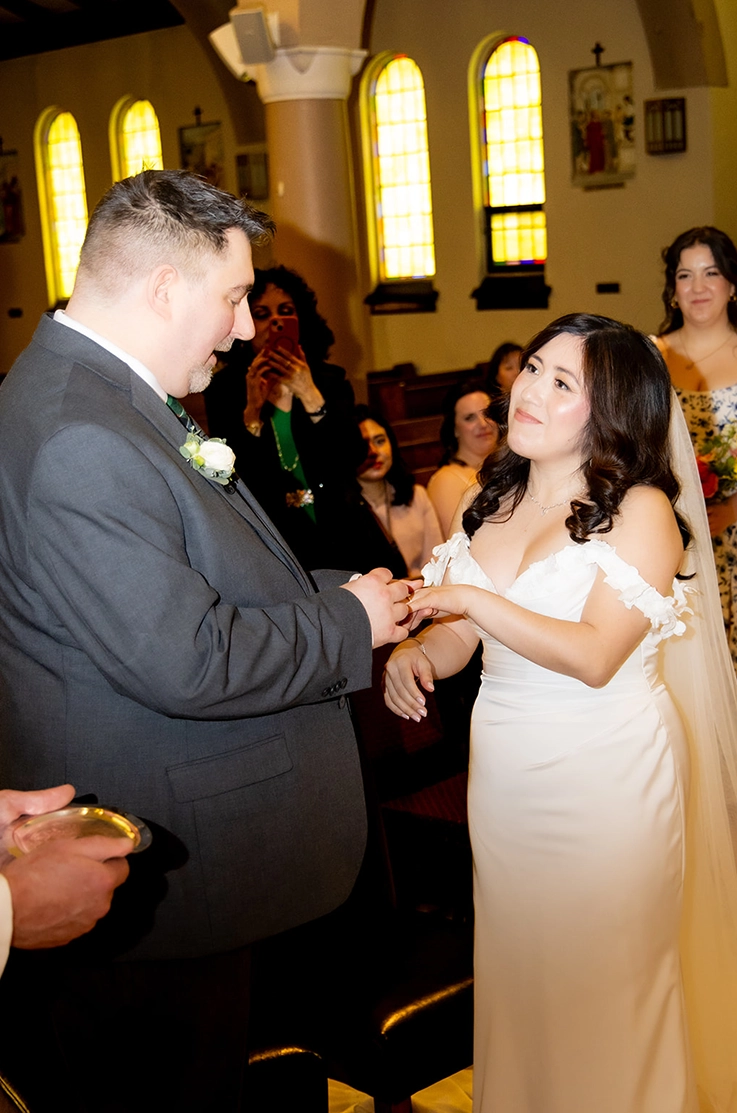 Bride in a strapless sweetheart neck gown with a draped bodice and lace detail, smiling at groom in church ceremony.