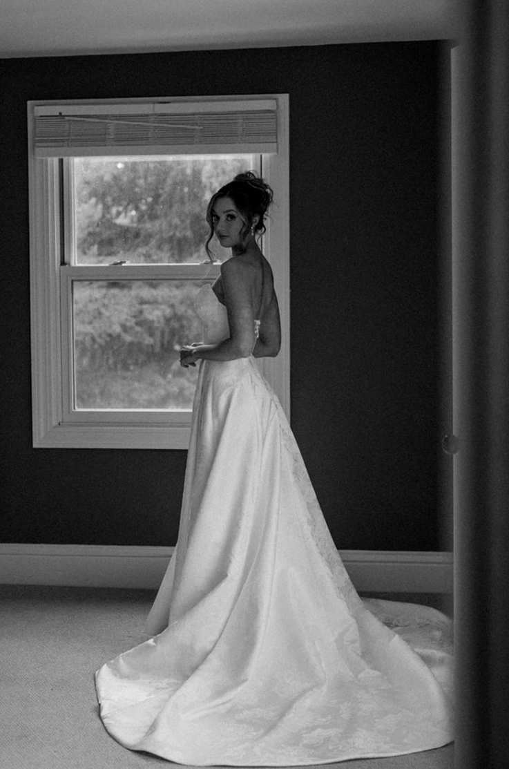 Bride in a strapless jacquard gown with a full skirt, looks over her shoulder in black and white indoors.