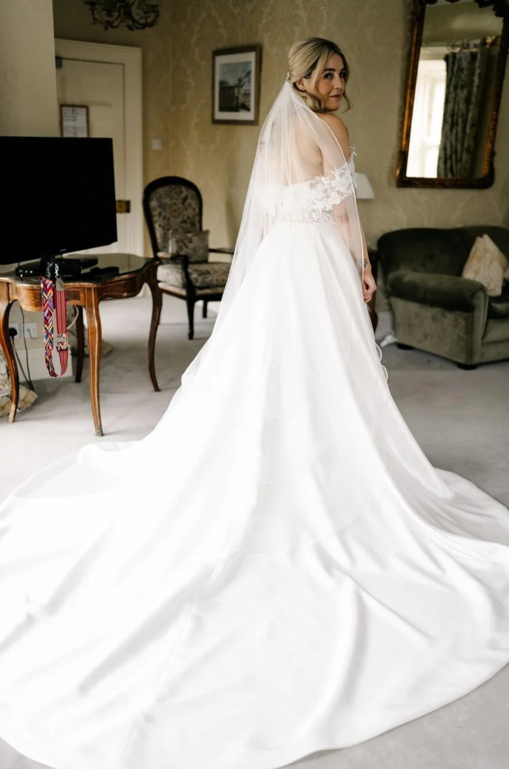 Bride poses looking over her shoulder in a mikado and lace flowing gown with a veil, in a luxurious manor suite.