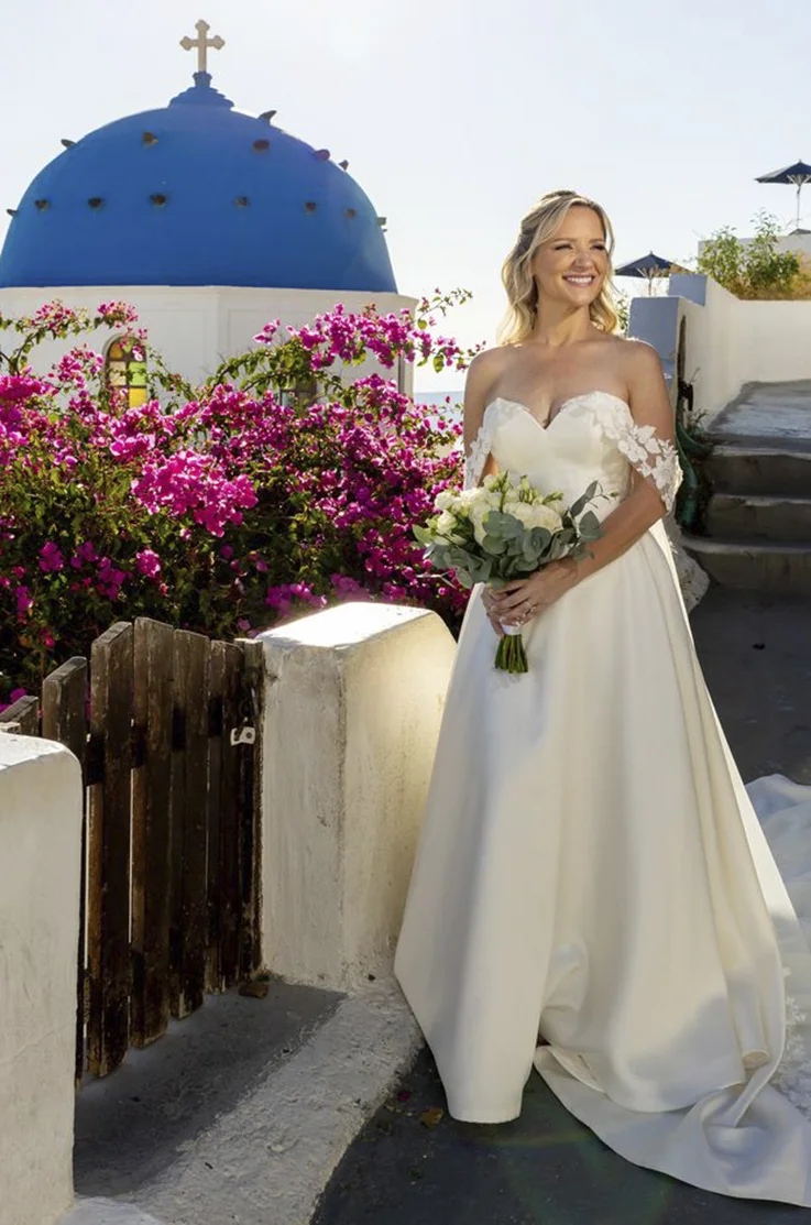 Smiling bride in a Mikado bodice gown with sequin lace detail, holding a bouquet on a Greek island. 