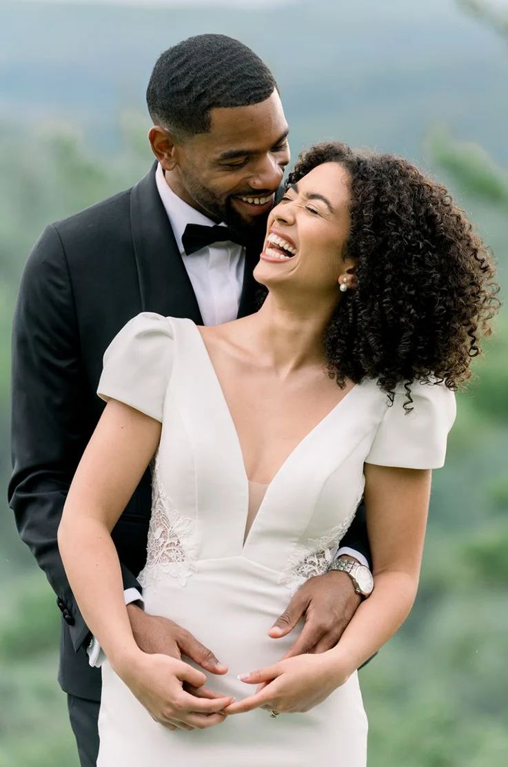 Close-up of groom holding his bride in an embrace in a plunging neck crepe gown with lace side cutouts. 